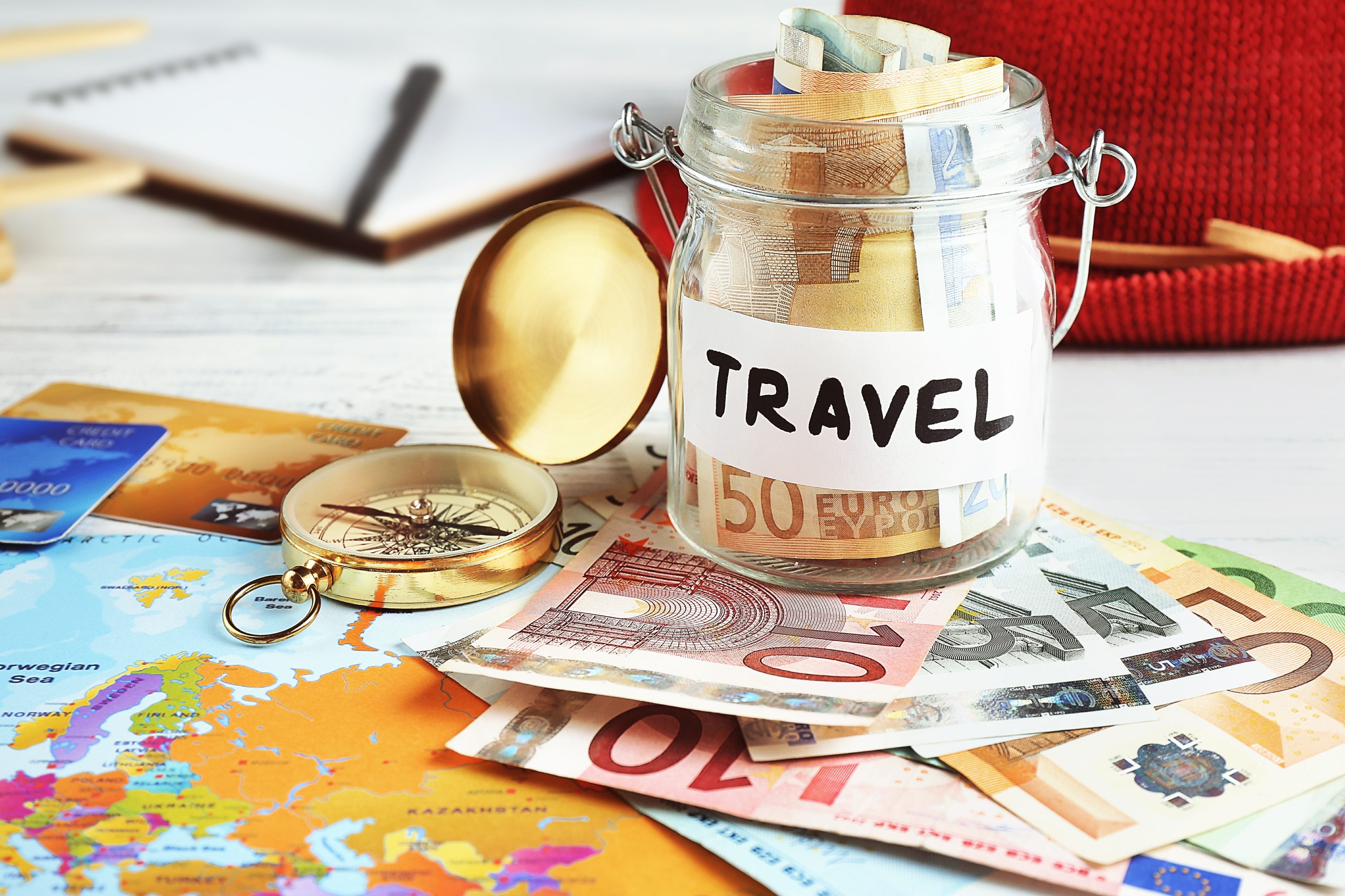 Travel money savings in a glass jar with compass, map and hat