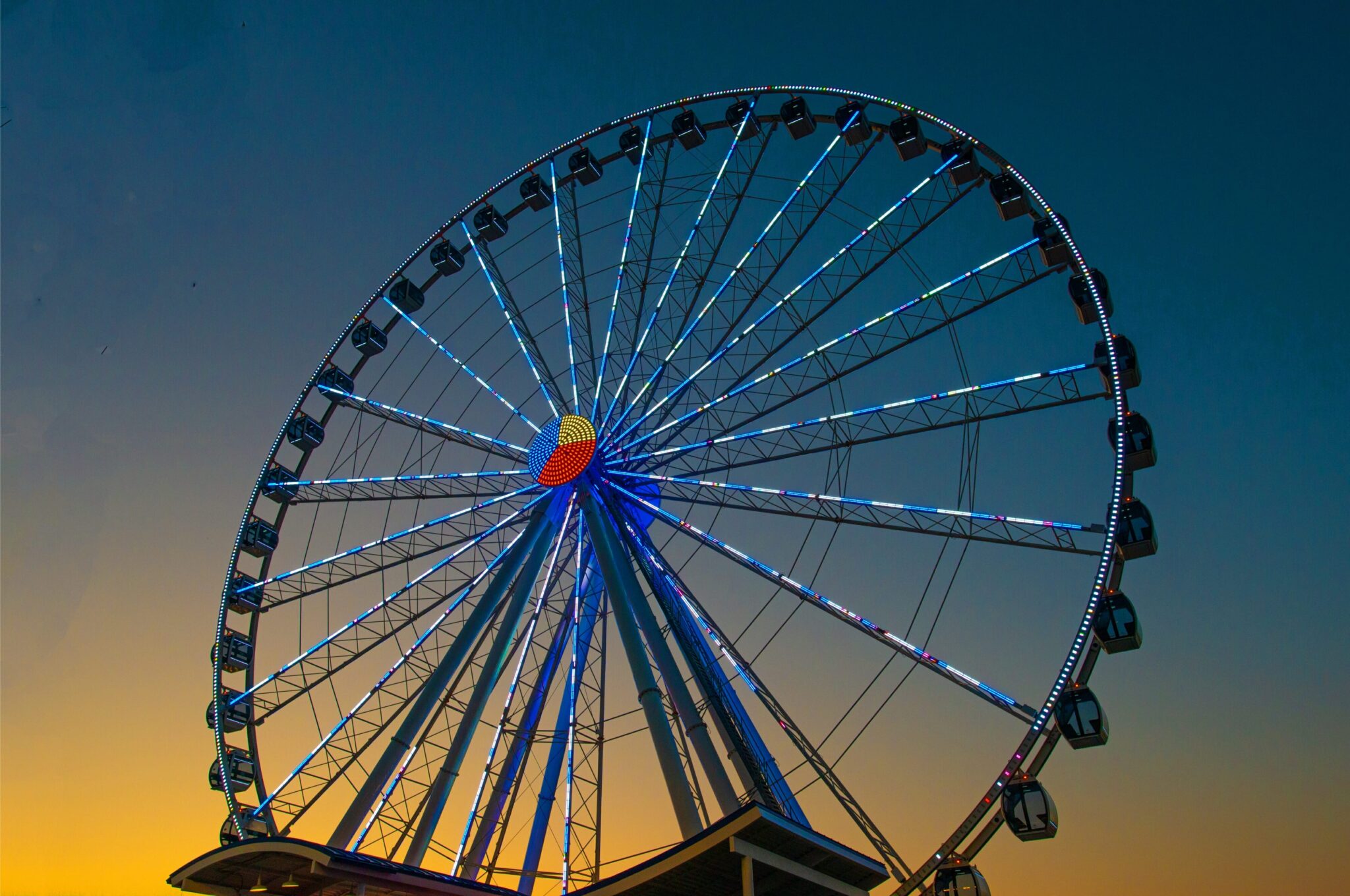 A vibrant ferris wheel illuminated against a picturesque sunset backdrop