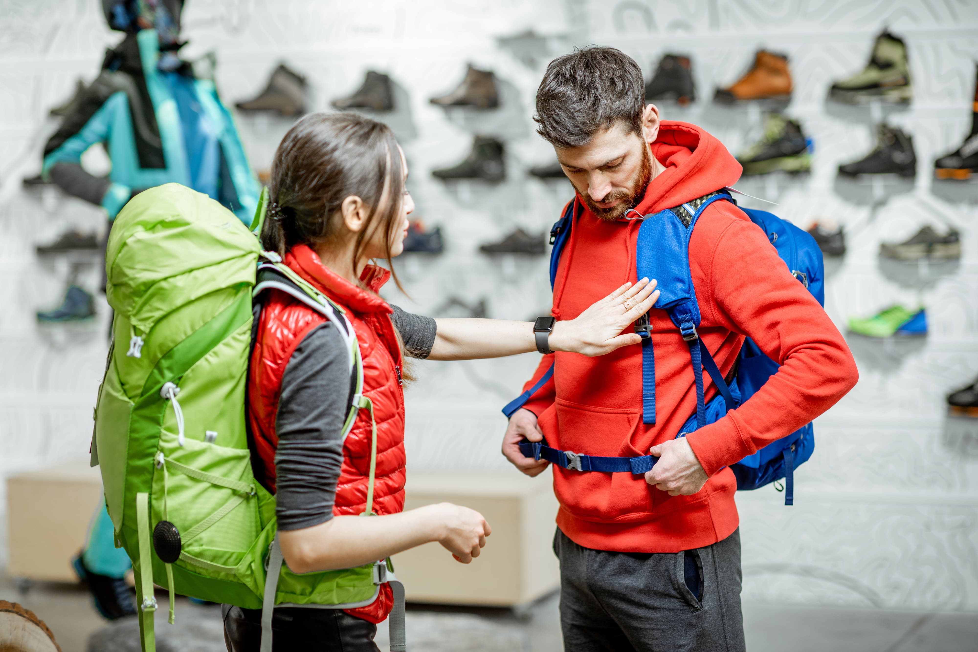 Young couple of travelers trying new backpacks in the shop with sports clothes and equipment
